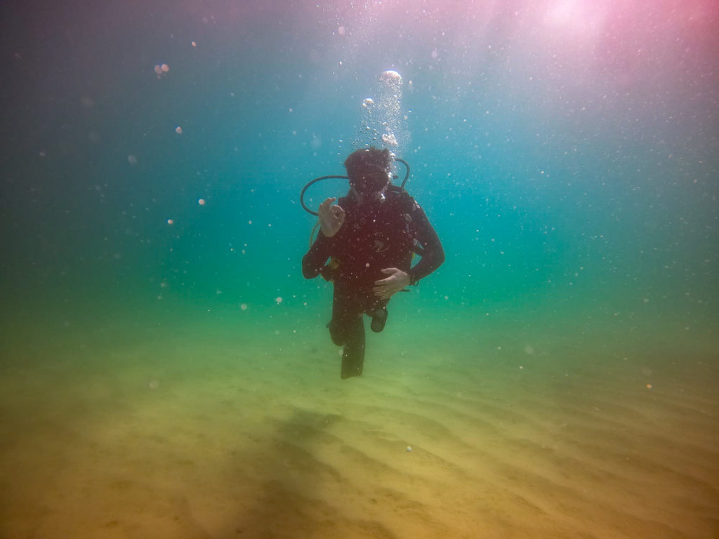 A submerged SCUBA diver makes the OK symbol at a photographer.