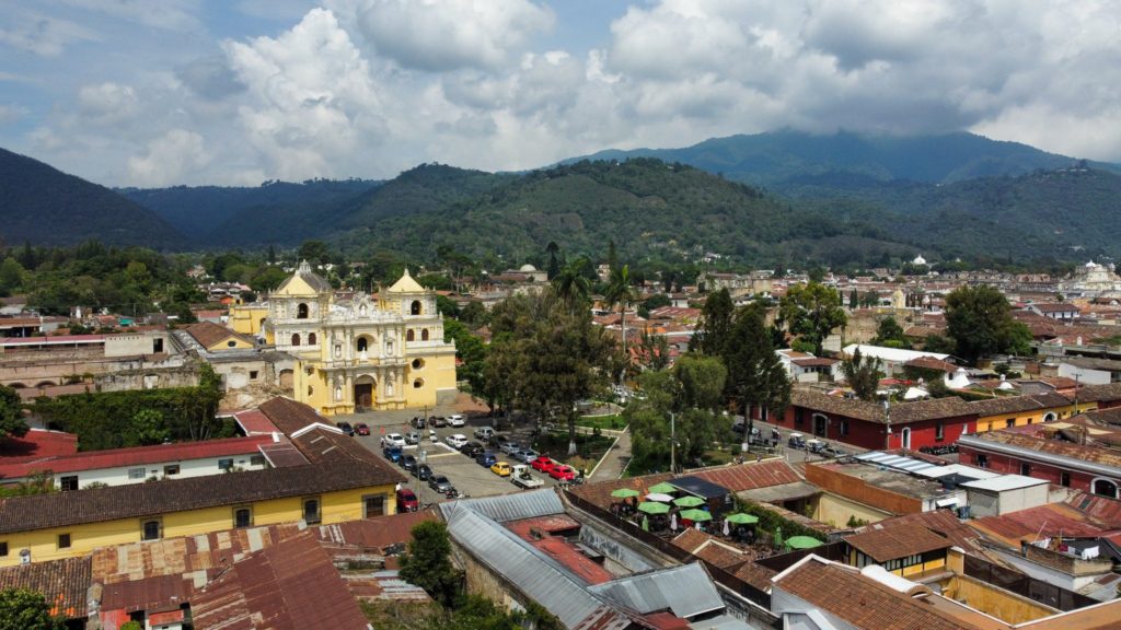 Antigua, Guatemala town with yellow church in front of mountains.