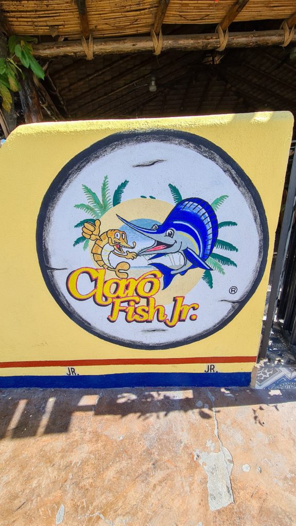 The entrance to Claro Fish Jr has a painted sign with the restaurant's logo - a shrimp and a marlin.