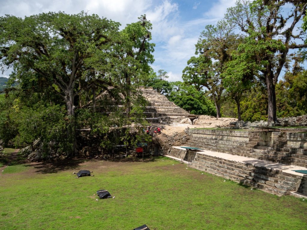 A view of one of the larger pyramid structures sitting behind trees. The buildings are many centuries old.