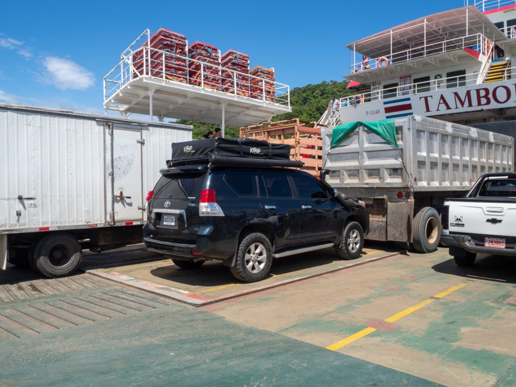 A camper car parked on a ferry behind a big truck.