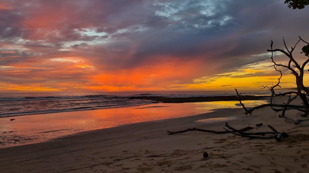 The red and orange light of sunset is reflected off the wet sand on a Costa Rican beach.