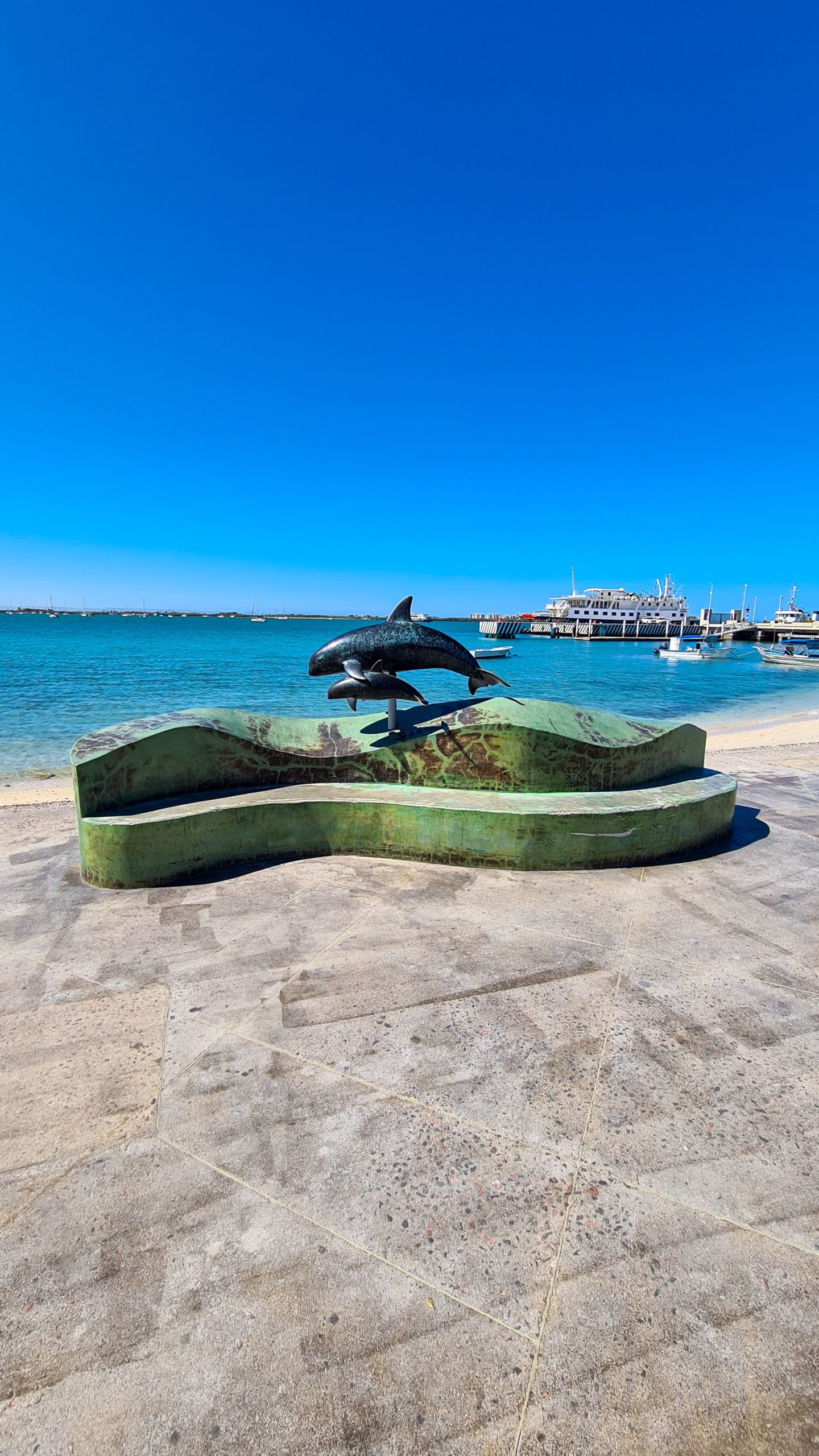 A metal statue of a mother and baby pilot whale swimming side-by-side.