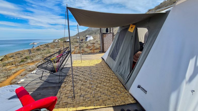 A tent sits on the side of a mountain with views of the sea.
