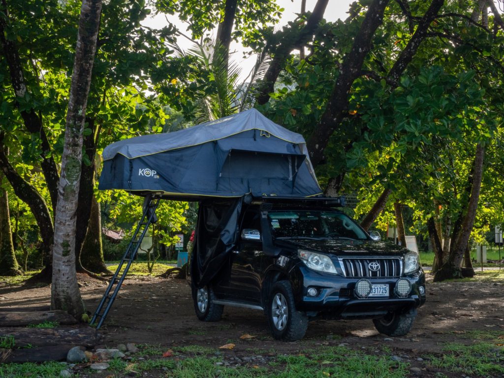 A car with a roof-top tent, parked by the beach.