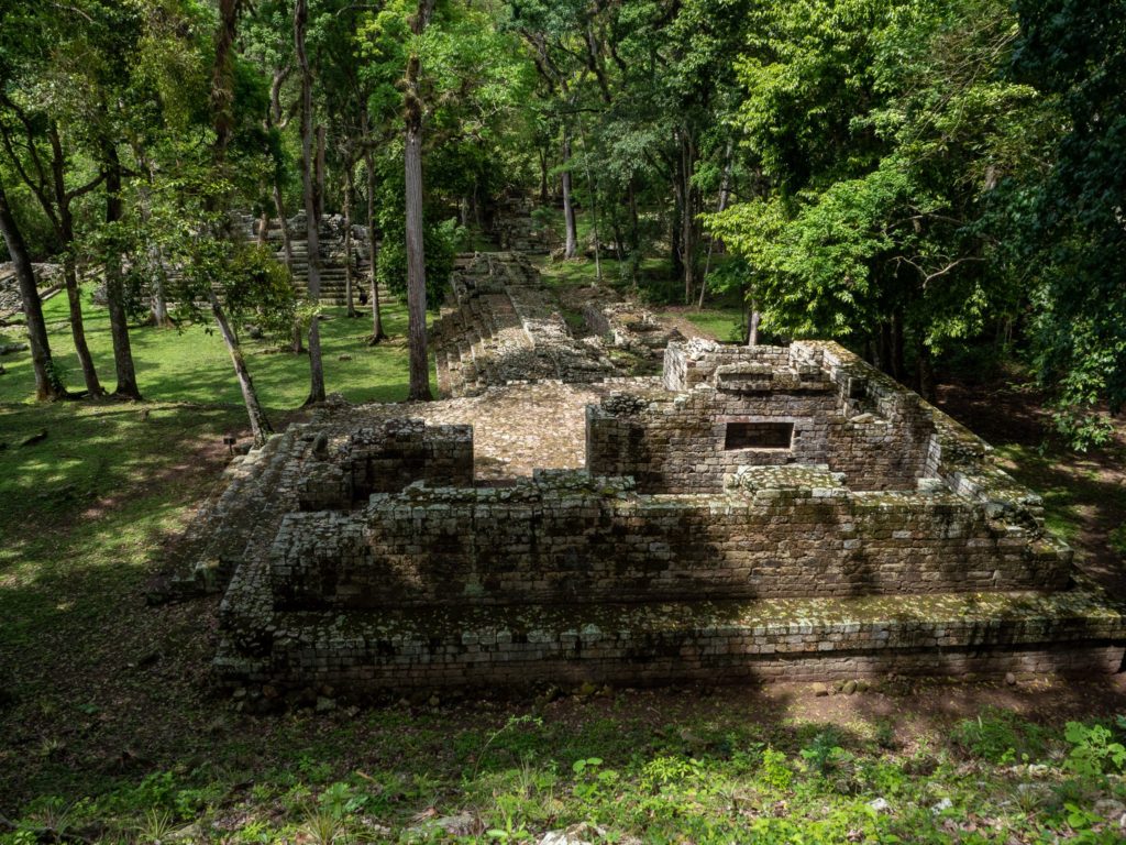 Several Mayan stone structures surrounded by greenery.