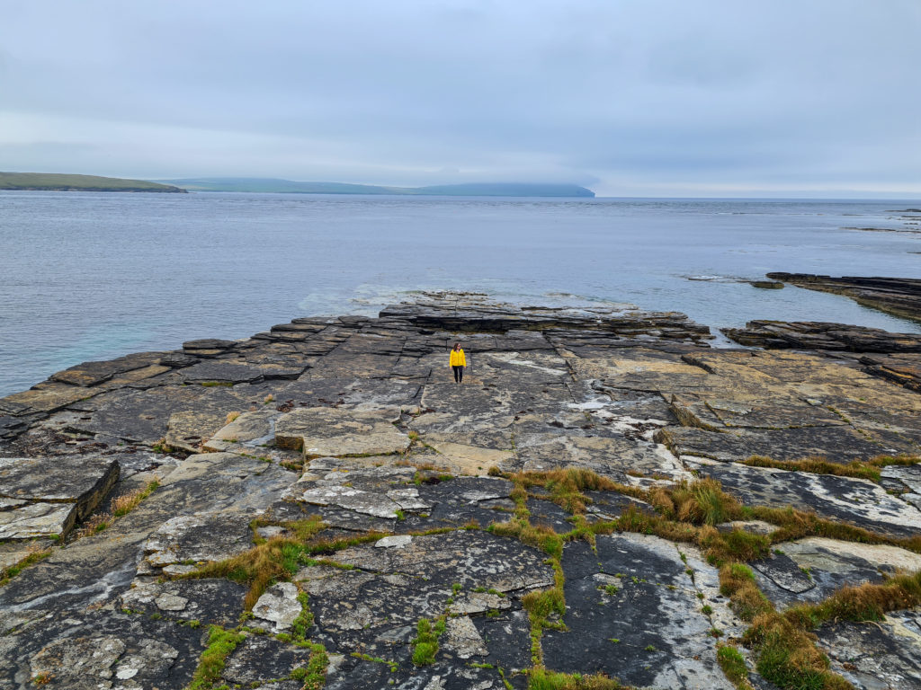 A girl in a bright yellow coat stands out on the rocks of Rousay.