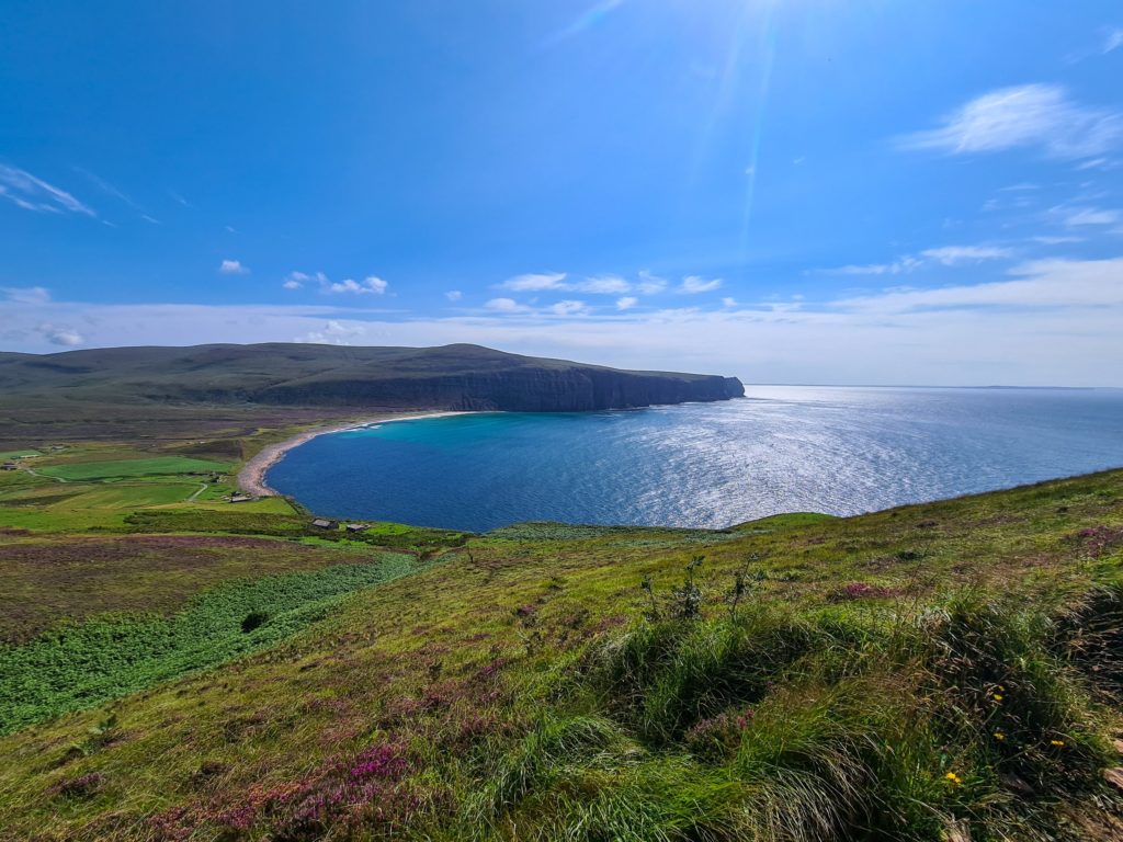 The sun reflects off a bright blue sea in a quiet, calm bay.