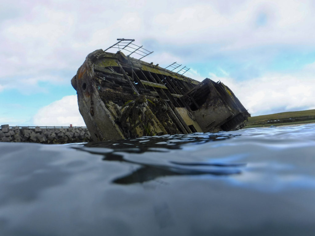 An old shipwreck seen from water level. The ship is rusted and covered in sea-weed.