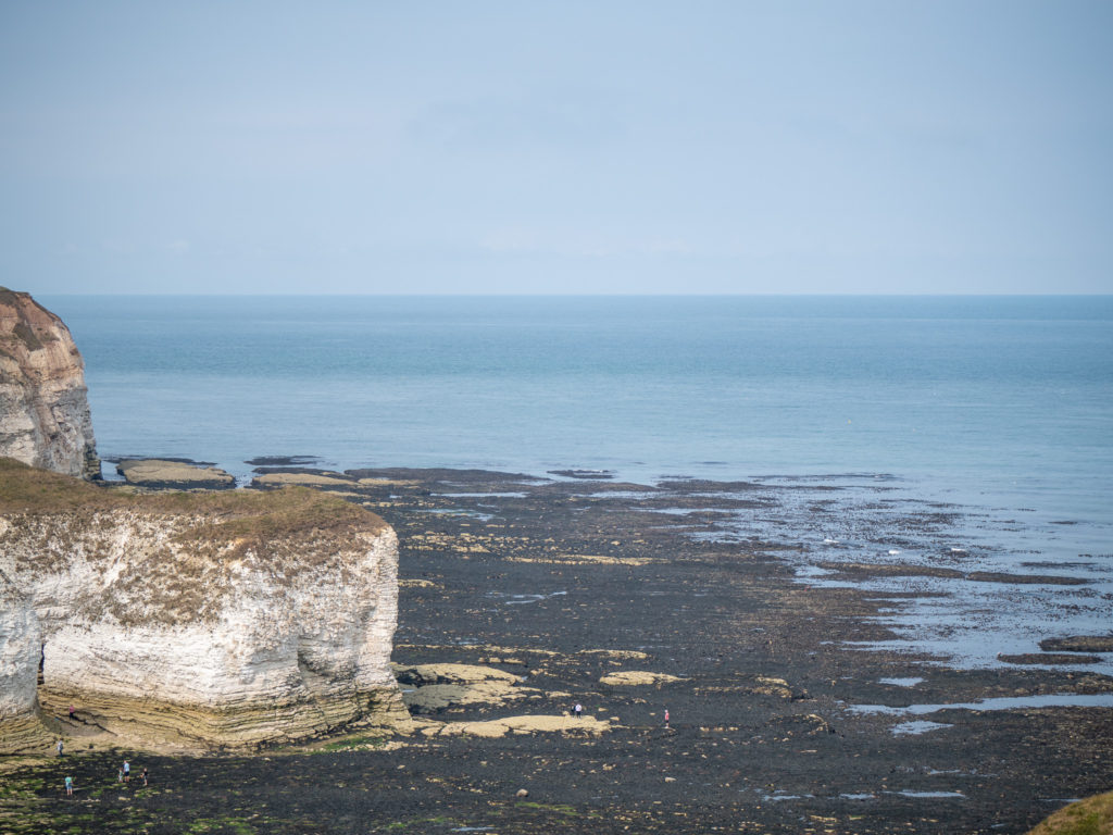The sea stretches out to the horizon. A few visitors wading on the rocks show of the sheer size of the cliff.