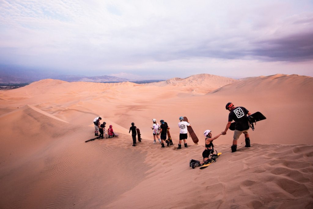 Tourists prepare to sandboard down sand dunes.