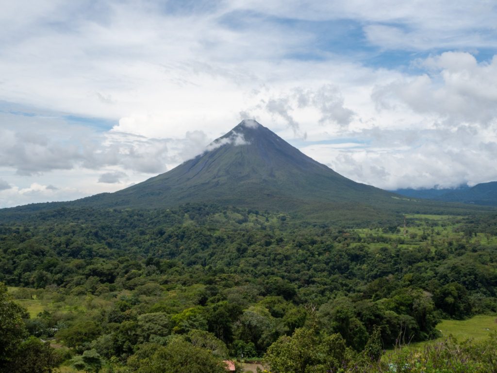 The impressive Arenal Volcano stretches high into the sky. The volcano itself and the surrounding area is a deep green.