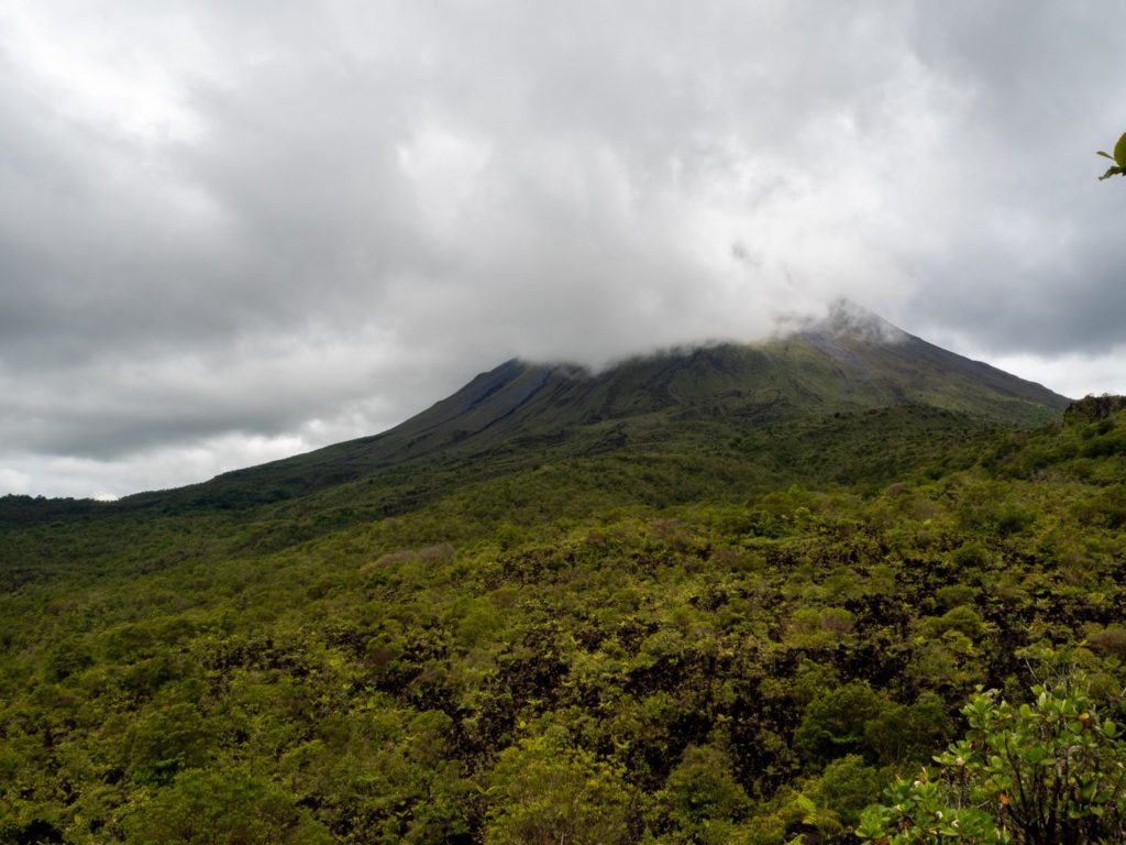 A thick layer of white cloud has started to cover Arenal Volcano. The sky is overcast.