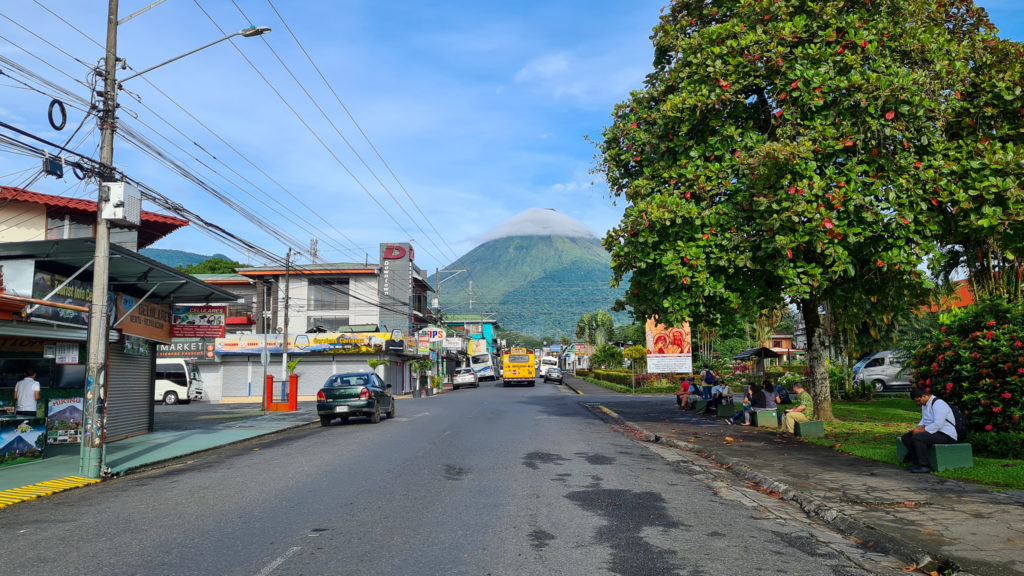 A town road leads to a volcano in the distance. A cloud sits on the top of the volcano.
