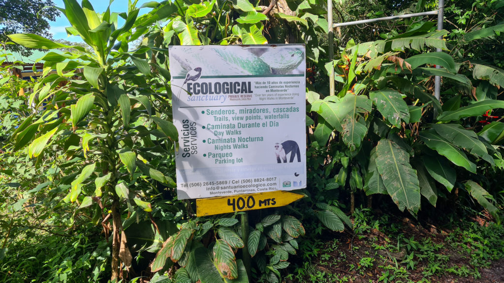 A white sign stands out amongst the greenery, it reads "Ecological Sanctuary, Private Reserve, Monteverde Costa Rica".