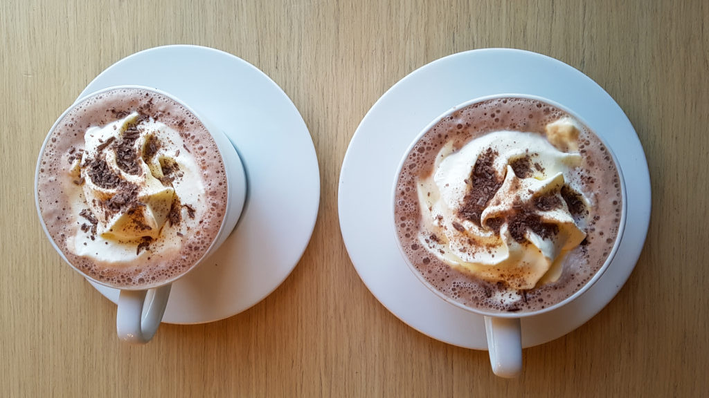 Two hot chocolates served with whipped cream and chocolate sprinkles.
