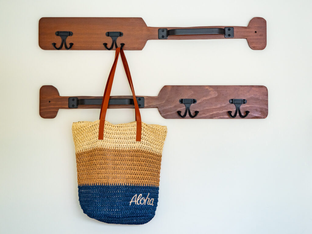 A beach bag hangs on a wall hanger fixed to wooden oars.