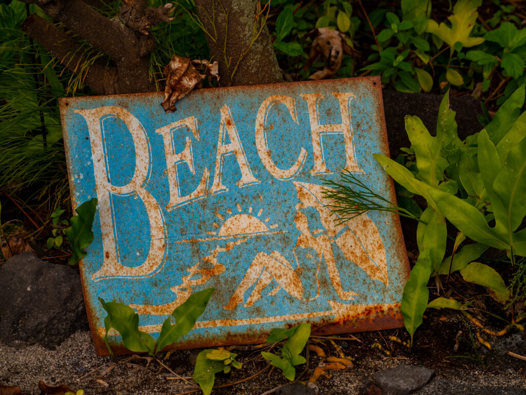 An old rusty reads "Beach" and depicts a lady with a parasol at the seaside.