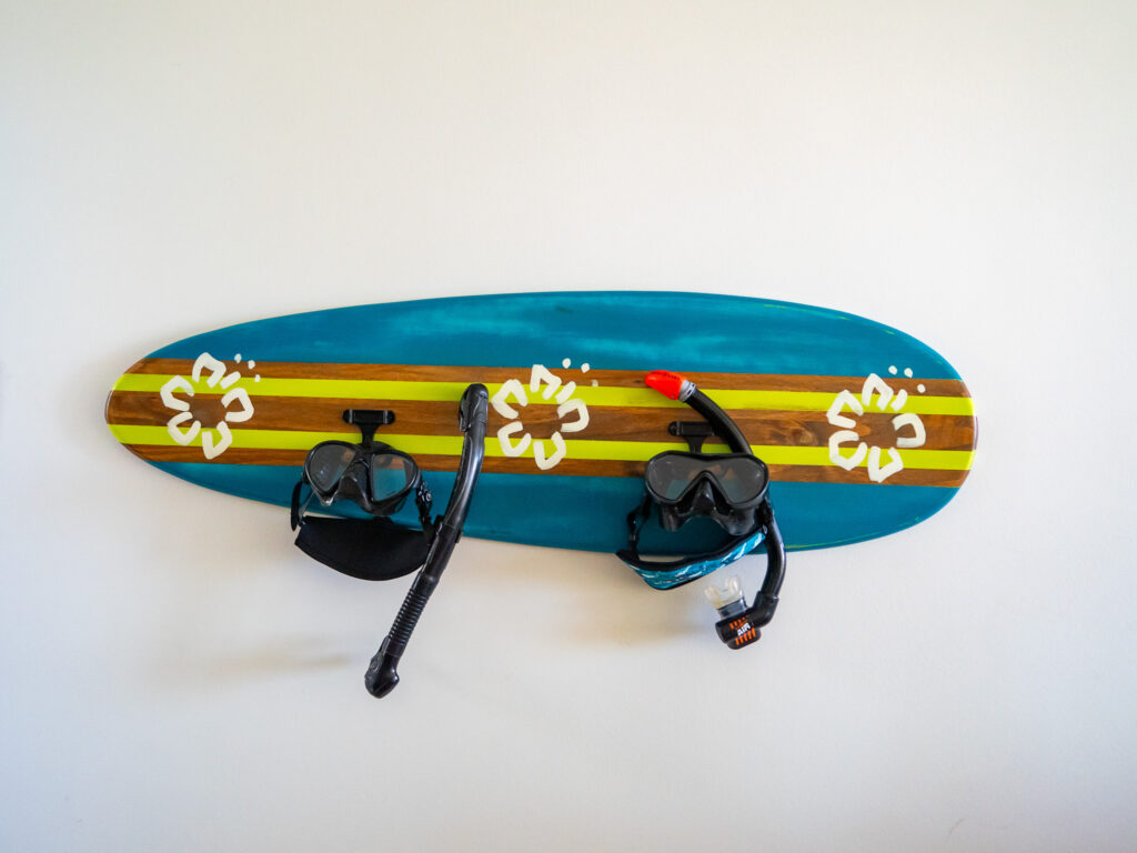 Two dive masks and snorkels hang on hooks ready for a day of snorkelling. The hooks are fixed into a decorated surf board.