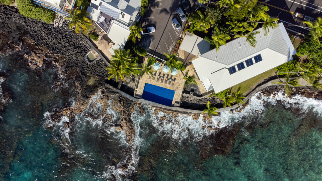 A view of Kona Tiki Hotel from the sky. We can clearly see parasols, palm trees and the solar panels lining the roof.