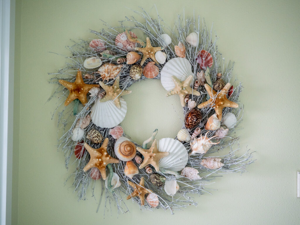 A close up of a sea-themed wreath. We see starfish and shells intertwined with thin white branches.