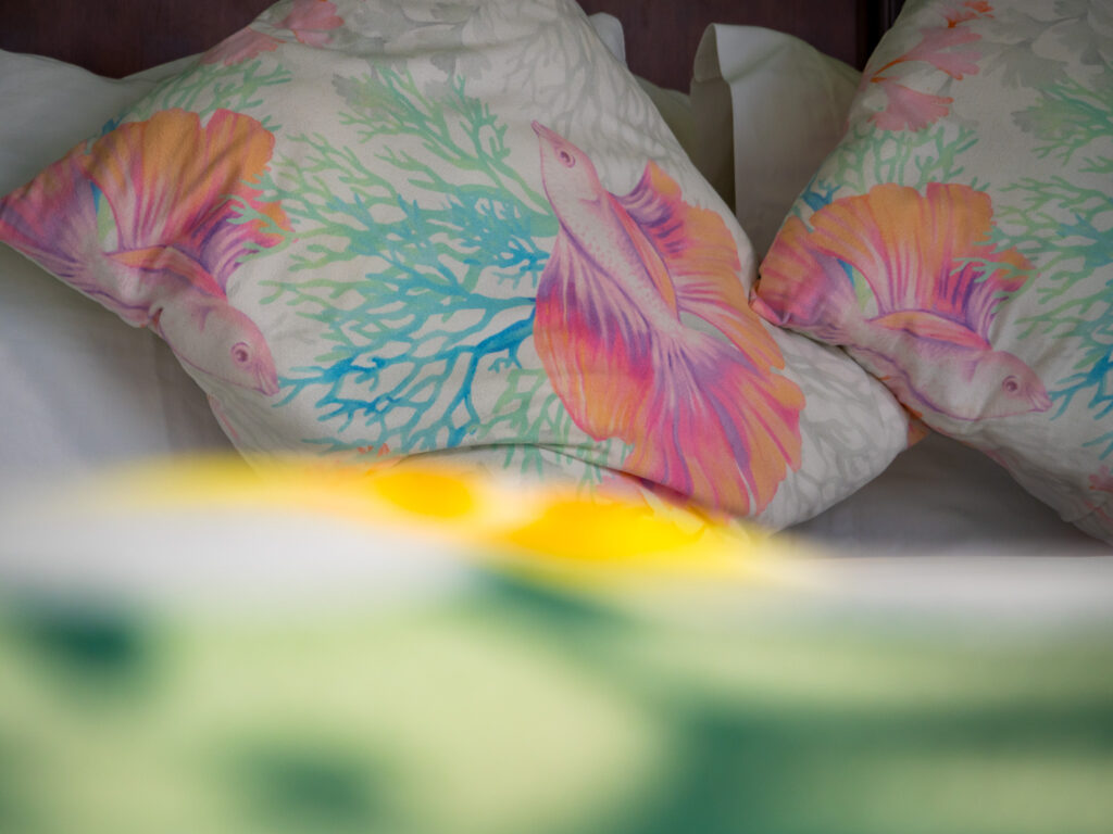 Painted images of tropical fish cover two pillows. The bed is made with clean white sheets.