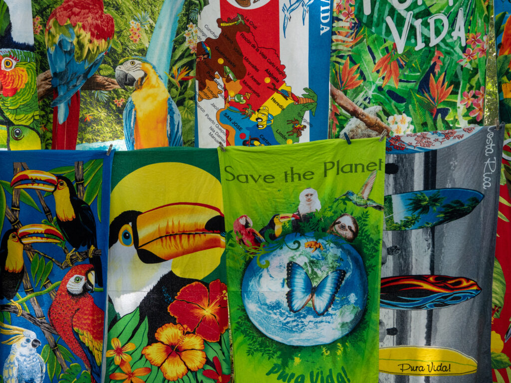 A close-up view of some towels on sale at a market in Costa Rica. There are many painted images of toucans and macaws along with other Costa Rican wildlife.