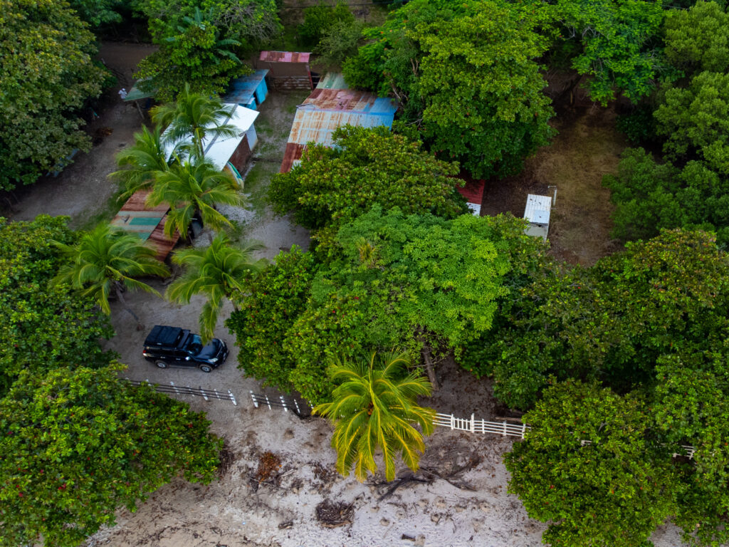 A drone shot of a campsite on the beach in Costa Rica. We can see a 4x4 camper rental parked in the tree-line.