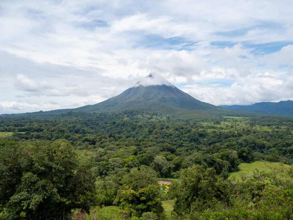 The impressive Arenal Volcano stretches high into the sky. The volcano itself and the surrounding area is a deep green.