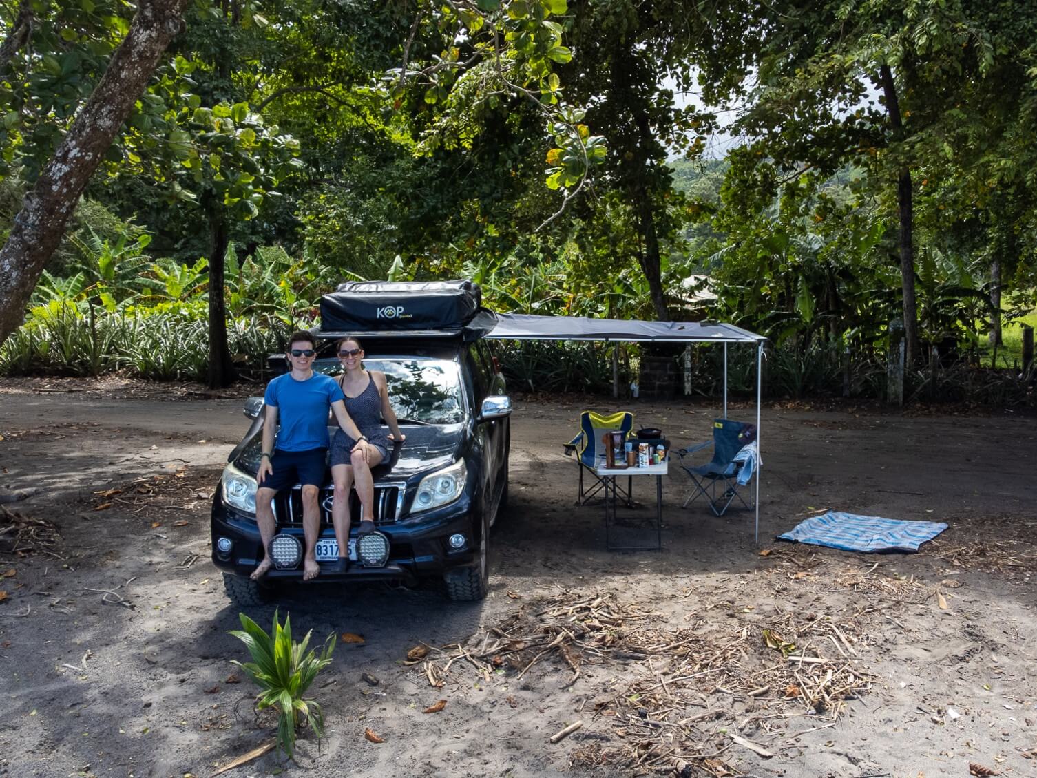 Dan and Lucy sit on the hood of a 4-wheel-drive camper car rental on a beach.