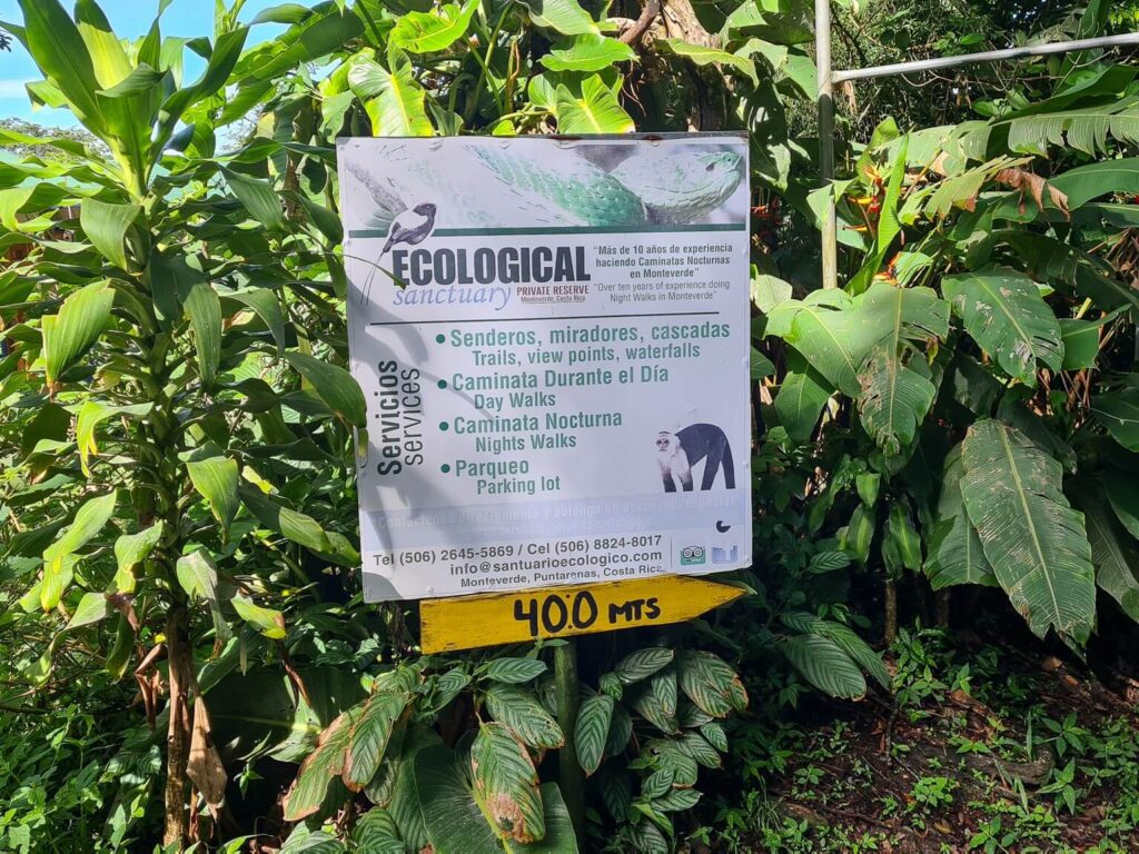 A white sign stands out amongst the greenery, it reads "Ecological Sanctuary, Private Reserve, Monteverde Costa Rica".