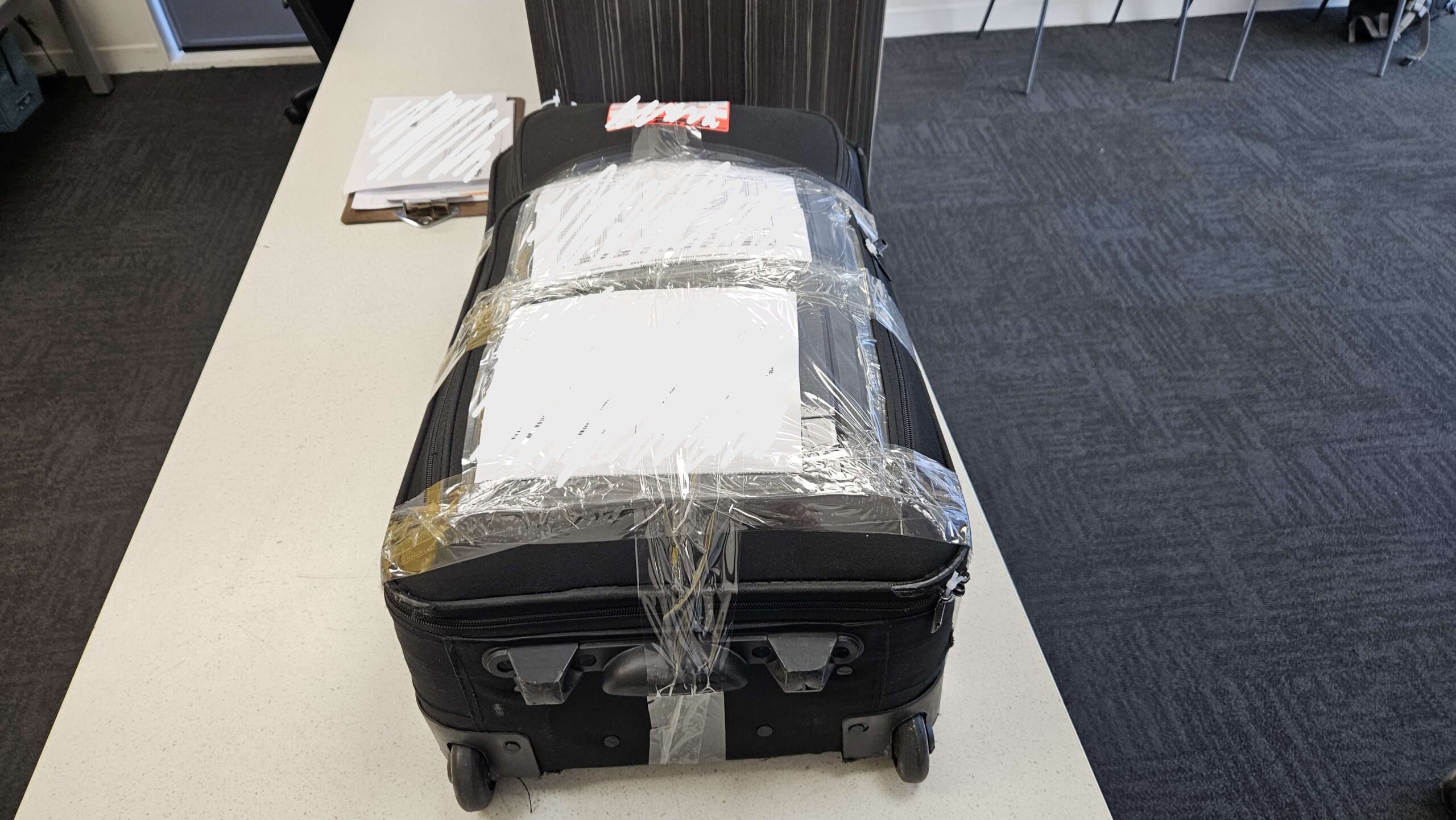 A suitcase lies on a service ready to be delivered. The suitcase is secured with tape and zip-ties.