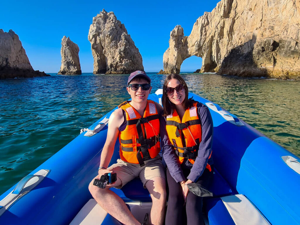 Dan and Lucy sit smiling on a tour boat. Behind them is the famous Arch of Cabo.