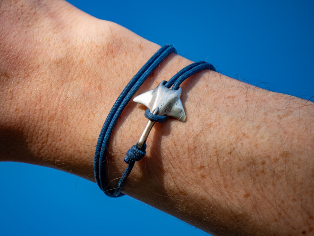 A silver clasp in the shape of a manta ray wrapped around Dan's wrist with blue twine.