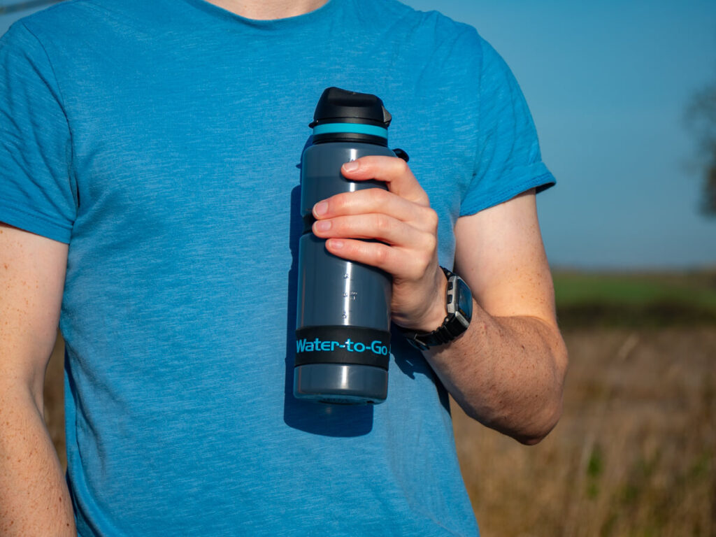 Dan holding a reusable water bottle in his hand. It has the words "Water-to-Go" printed across it in blue writing which matches Dan's top.