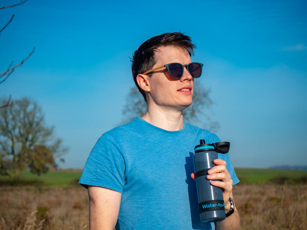 Dan looking out at the countryside in his sunglasses, holding a blue Water-to-Go water bottle.