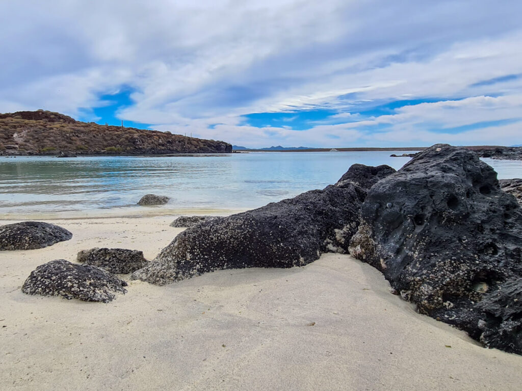 A white sand beach with volcanic rocks and clear blue water.