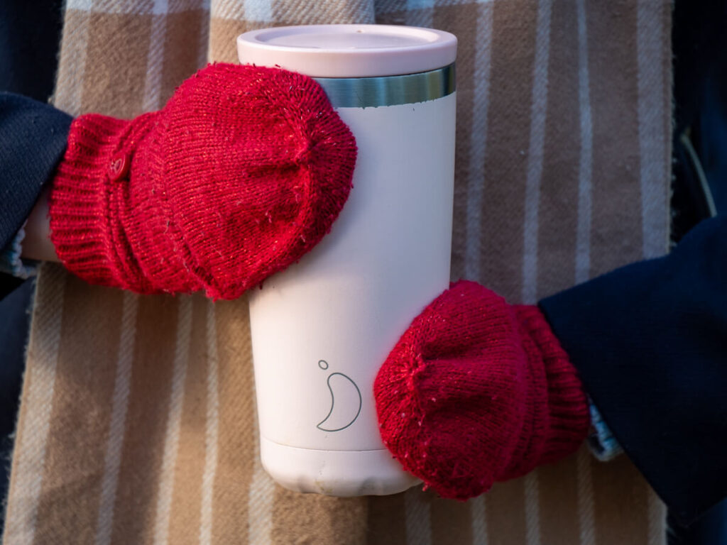 Lucy holding her pink Chilly's coffee cup with bright mitten-donned hands.