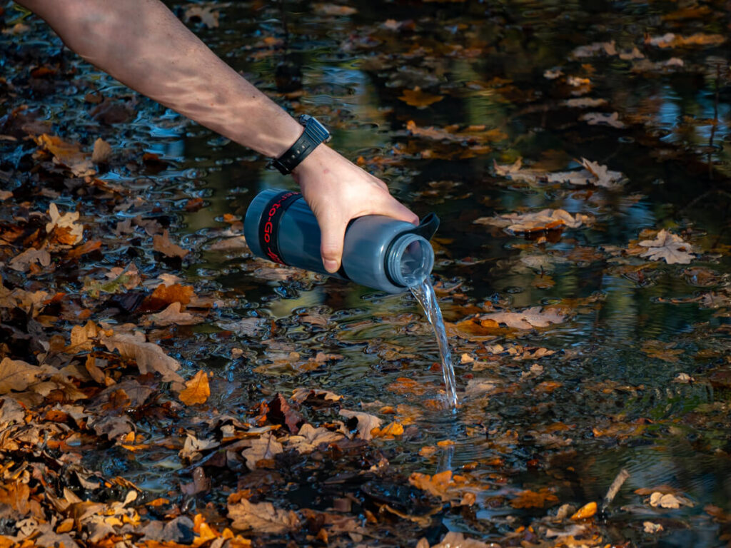 Pouring water into a nearby stream from a reusable active water bottle.