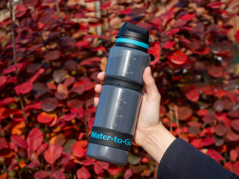 A Water-to-Go sugarcane bottle held in front of a bush of bright red leaves.