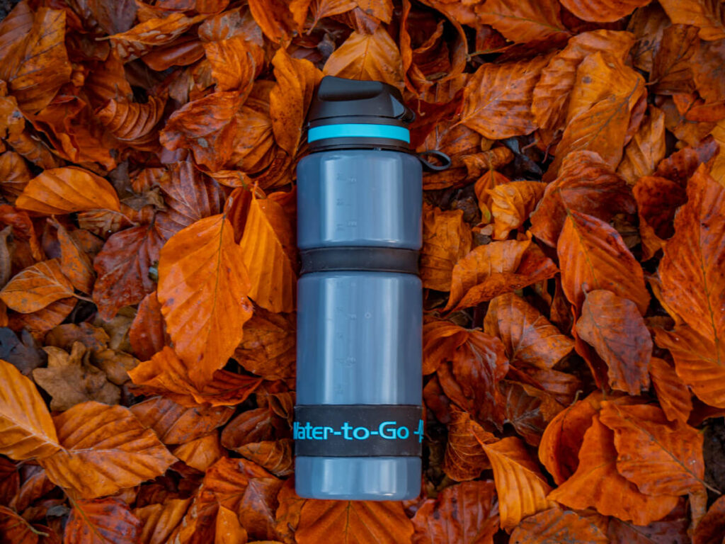 A filtered water bottle lying on a pile of bright orange leaves. The words "Water-to-Go" are inscribed across the front of the bottle.