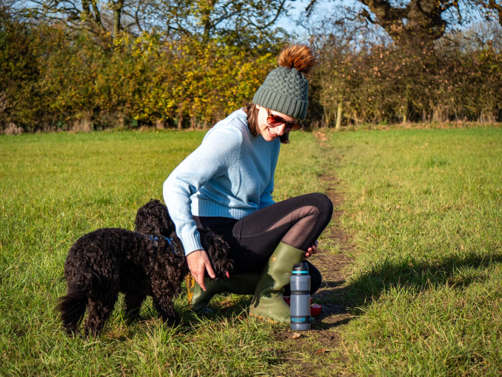 Two dogs greeting Lucy, one with its tongue out, as she bends down to pick up her water bottle.