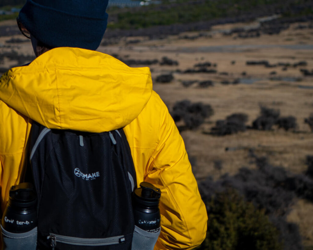 Lucy on a hike in a bright yellow coat. She is carrying a backpack with a Water-to-Go bottle slotted into each drinks holder.