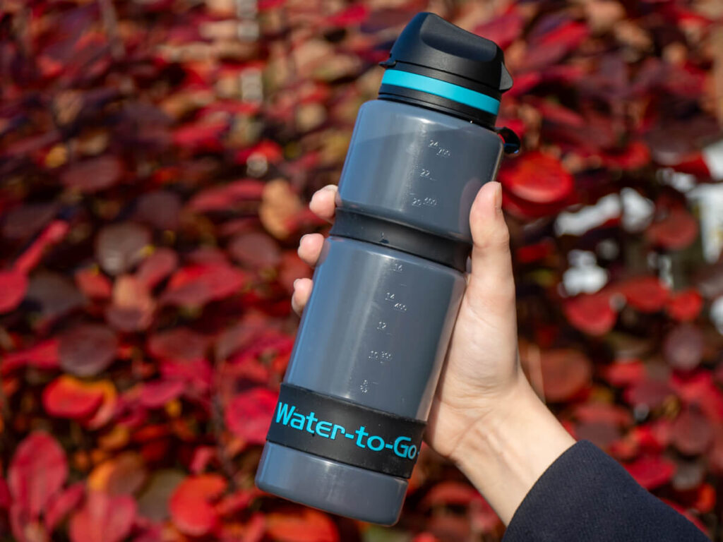 Lucy holding an active water bottle in front of a scene of autumn leaves.