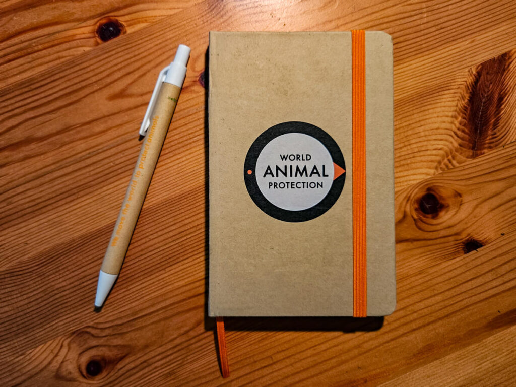 A pen and notepad made from recycled materials. The notepad has "World Animal Protection" branded on the front, and the pen has the words "We move the world to protect animals" printed along it.