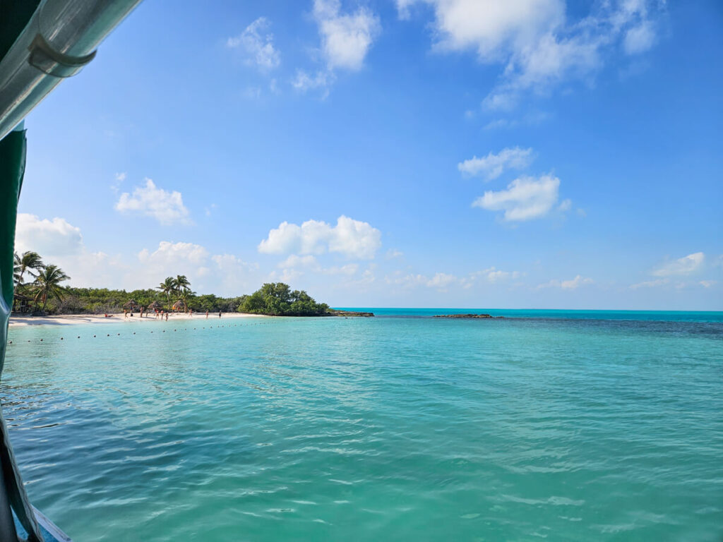 Isla Contoy as viewed from a boat. There are a few people stood on a white sand beach and the water is very clear.
