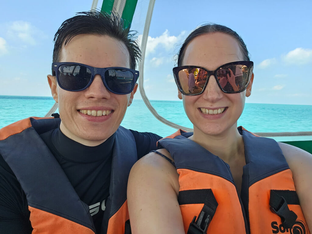 Dan and Lucy smiling at the camera after a wet boat ride. Their hair and sunglasses have been splashed by the ocean.