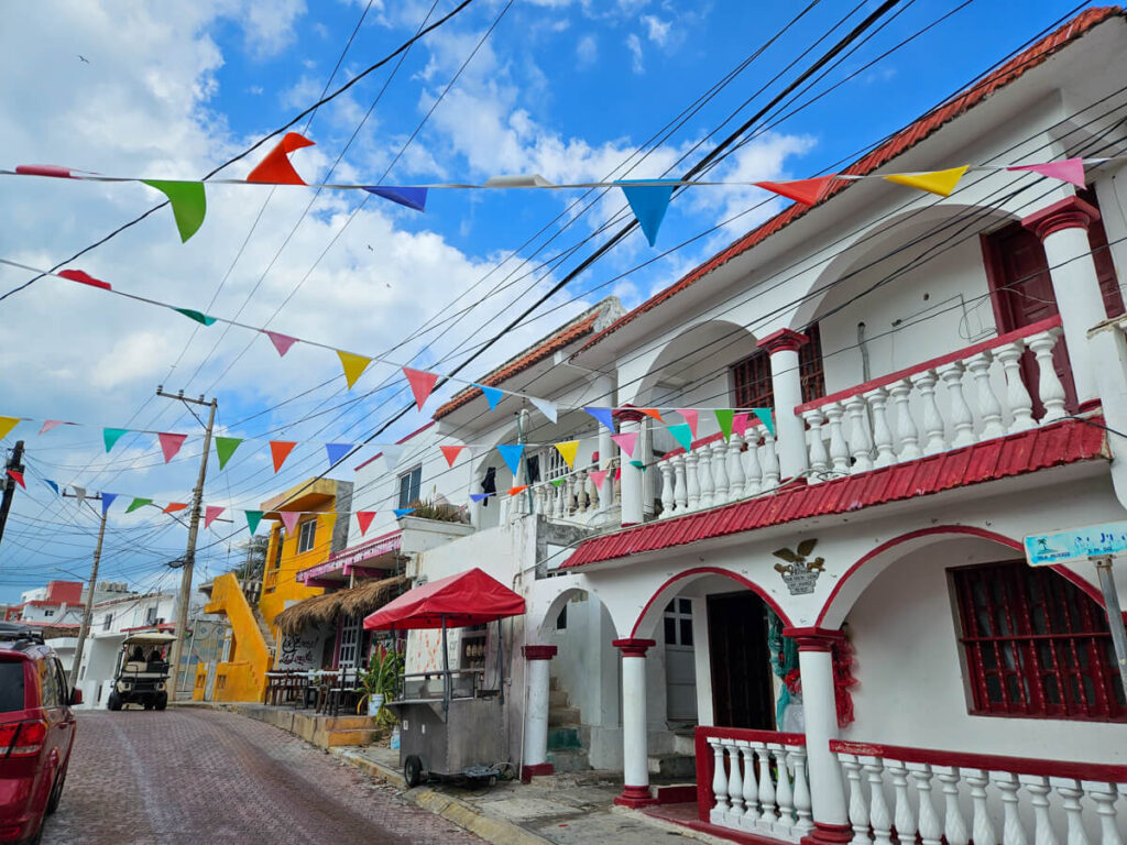 Colourful bunting hanging from buildings in Isla Mujeres. The street is cobbled for cars and gold carts to drive over.