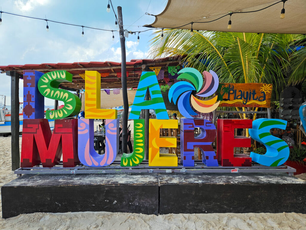 A colourful sign that says "Isla Mujeres" under a sunny sky.